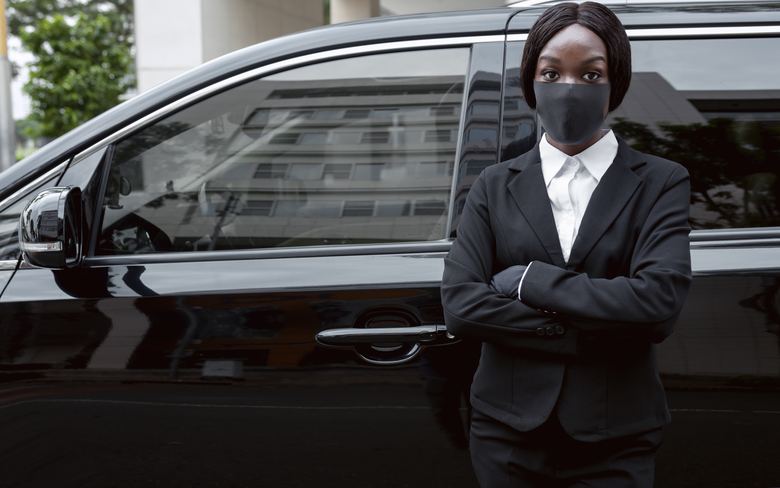 Chauffeur en costume sombre devant un véhicule funéraire noir